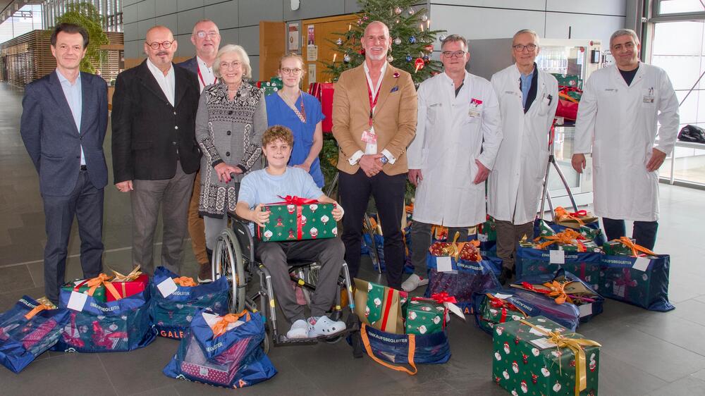 150 Geschenke für die kleinen Patientinnen und Patienten - Michael Zielke (M.), Filialgeschäftsführer bei GALERIA Karstadt Kaufhof GmbH, und der kaufmännische Leiter Stefan Tröndle (3.v.l.) haben dies an die Vorstände des Klinikums Janko Haft und Prof. Michael Albrecht sowie Mediziner der Kinderklinik, Kinderchirurgie und Kinderonkologie übergeben. Der 13-jährige Benny freut sich darüber. Foto: UKD/Marc Eisele