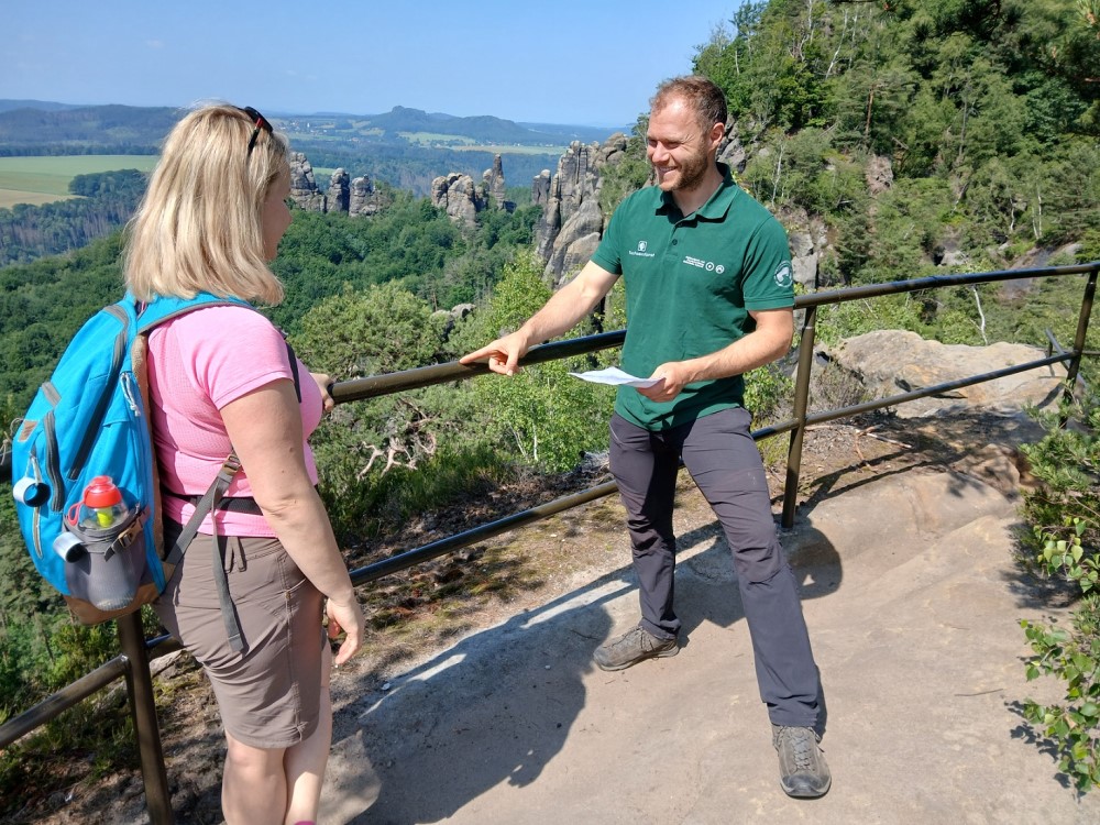 Martin Aulitzky (r.), Sachbearbeiter für Besuchereinrichtungen bei der Nationalpark- und Forstverwaltung von Sachsenforst, erläutert einer Wanderin aus Polen den Erhalt des Geländers entlang des Schrammsteingratwegs durch die Nationalpark- und Forstverwaltung, das einen frischen Korrosionsschutz-Anstrich erhalten hat.   Foto: K. Partzsch